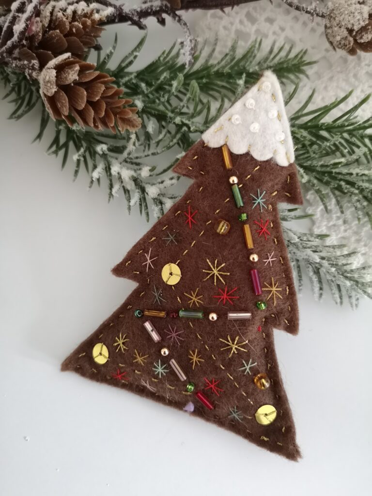Here at Anamae, we love Christmas crafts that make a difference. A beautiful Christmas ornament for your table decorations or mantel is always that little something that makes everything so perfect. This beautiful Christmas tree is made of felt and filled with polyester, making it look like a cushion. It is a pretty brown tree with white felt snow on top, decorated with glass beads and small snowflakes embroidered with gold thread. The back is decorated with flower-shaped sequins. They have been one of my favorite ornaments for so long, I could not wait to share them with you.