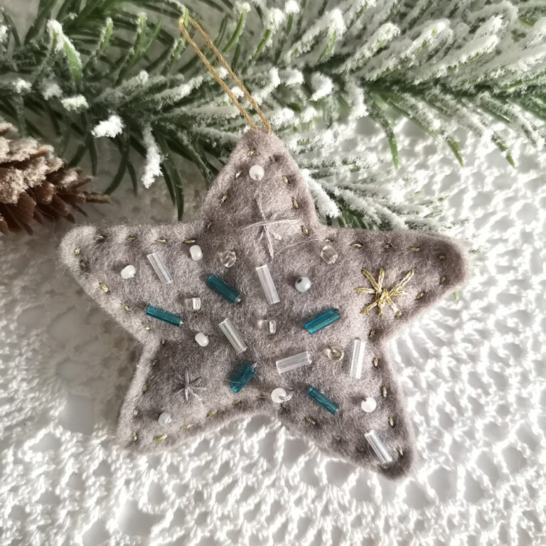 The star is made of wool felt and filled with polyester, making it look like a pillow. It is a beautiful soft gray and decorated with glass beads and small snowflakes embroidered with gold thread. The back is decorated with fuchsia and purple sequins. These beautiful felt Christmas stars have been one of my favorite ornaments for so long, I could not wait any longer to make them and share them with you.