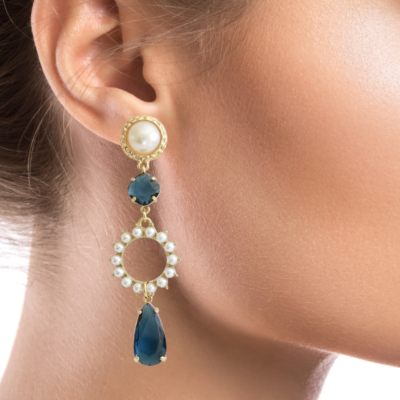 Enhance your look with these sophisticated and timeless earrings, featuring a duo of exquisite deep blue crystals (one round and one drop-shaped) adorning a golden circle embellished with pearls. A hammered gold frame encases the pearl stud, adding to its appeal. These earrings are a great choice for weddings or other formal events.