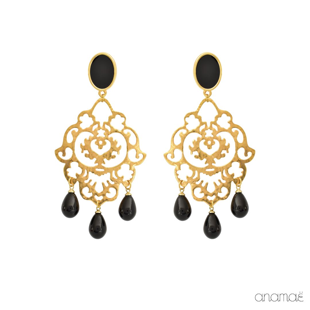 These elegant earrings are made from brass and 24k gold-plated. The intricate filigree motifs used in their design make them look like lace. The studs are oval and feature a combination of gold and black. The gold surface of the studs is covered with a glossy enamel coating, giving them a polished finish. The filigree motifs are adorned with three black teardrops, which add a touch of movement. The luxurious gold plating contrasts beautifully with the striking black enamel and teardrops, making these earrings suitable for any formal occasion. With their sophisticated and elegant appearance, these earrings are a versatile accessory that will complement any outfit.